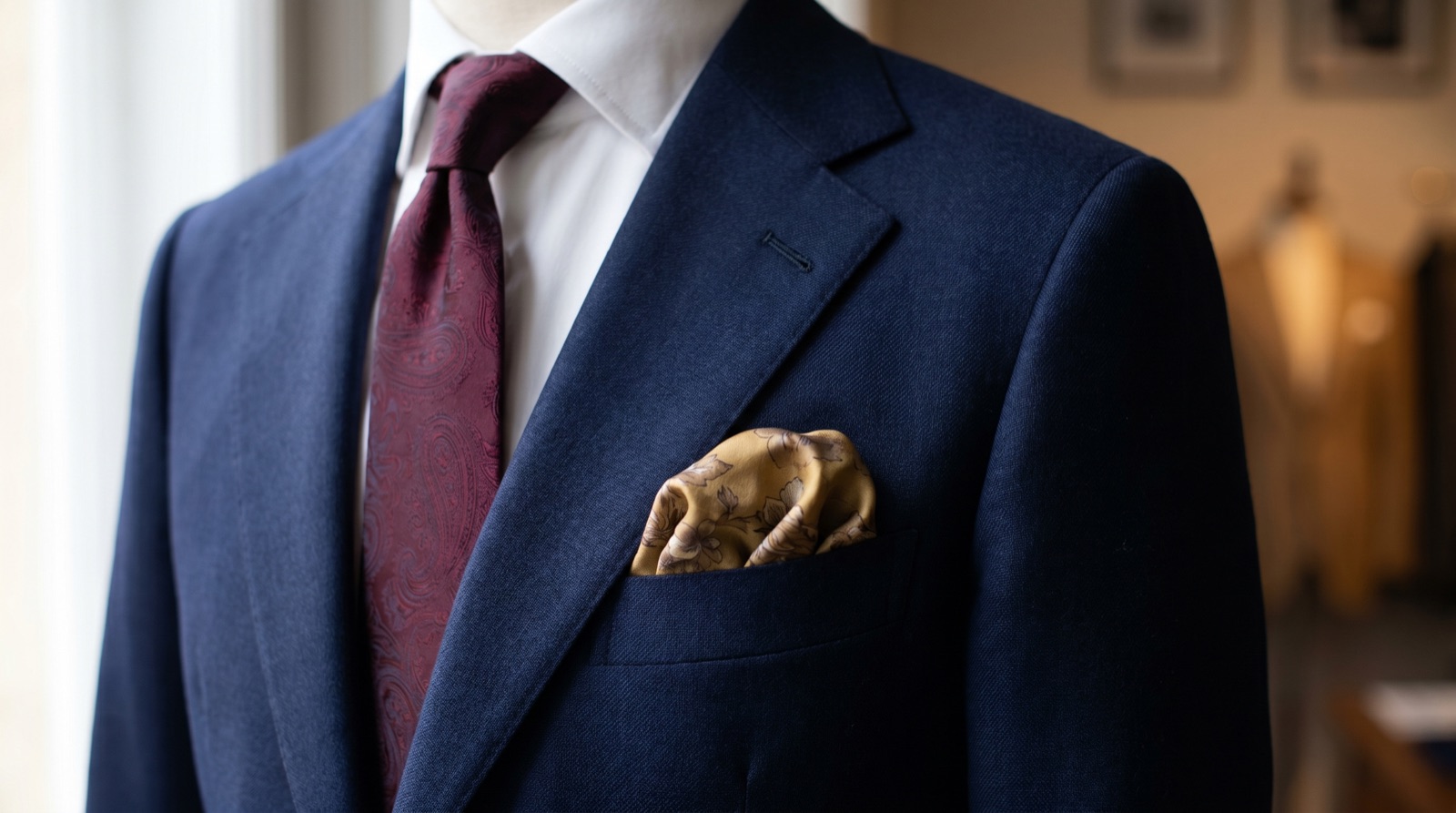 Navy suit chest with a burgundy tie and coordinating antique gold pocket square